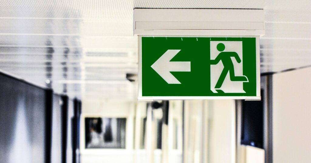 Panneau de signalisation d'évacuation d'urgence vert avec une flèche à gauche et un pictogramme d'une personne qui court, symbolisant la sécurité et la prévention des risques industriels.