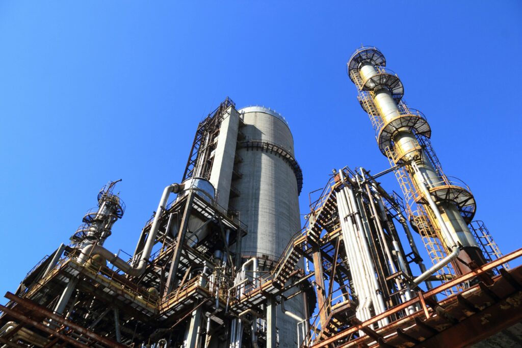 Vue en contre-plongée d'une grande installation industrielle complexe avec tours, silos et tuyauteries, symbolisant les environnements à haut risque d'explosion (Zone ATEX).